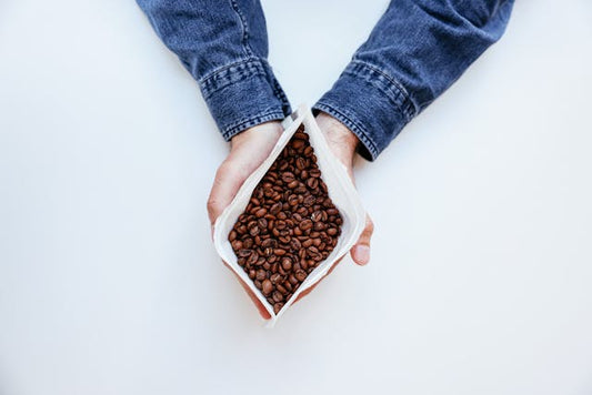 2 handen die een witte zak met gebrande koffie bonen vast houden